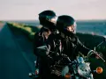 Coppia in moto romantica, con caschi neri, giacche di pelle, su una strada panoramica al tramonto.