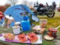 Colazione da campeggio in moto: caffè dalla moka, pane con marmellata e castagne, con tenda e moto sullo sfondo.