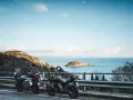 Due moto parcheggiate con vista sul mare e un'isola, con un rudere sulla collina. Un'avventura in **Argentario in moto** attende.