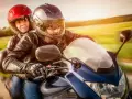 Coppia in moto, con lui alla guida e lei dietro, entrambi con caschi e giacche di pelle. Un'immagine che evoca la libertà di come guidare una moto.