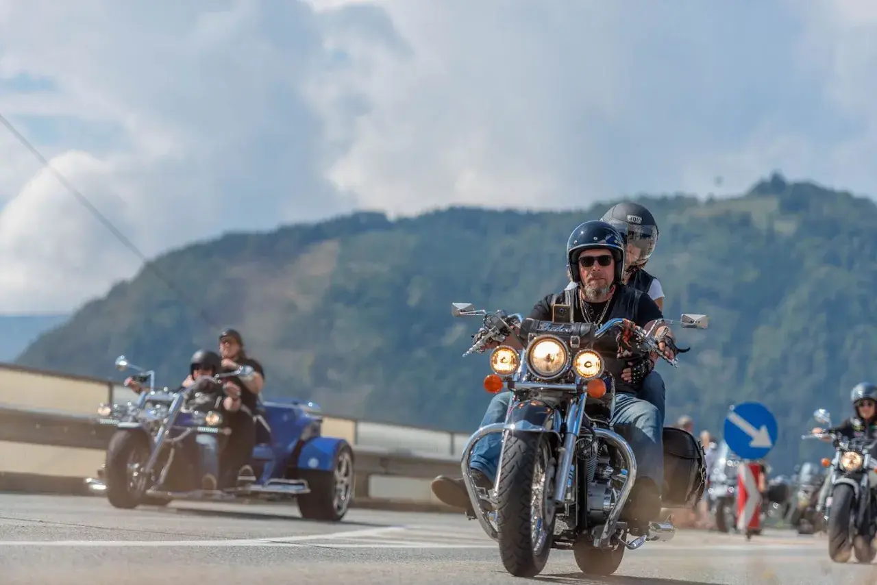 Coppie in moto e un trike sfrecciano su una strada panoramica, parte della European Bike Week.