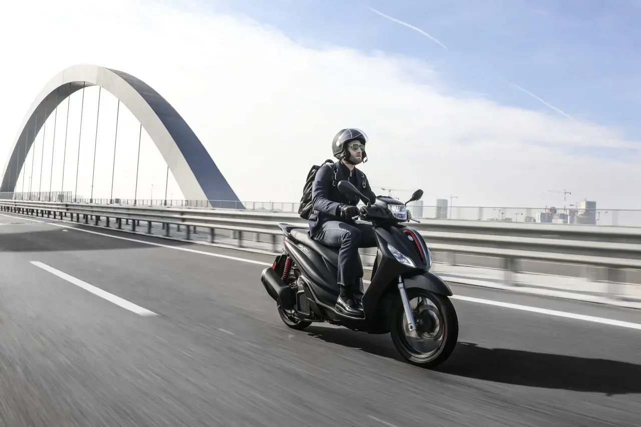 Uomo in moto sfreccia sull'autostrada, con un grande ponte ad arco sullo sfondo. La libertà di viaggiare in moto.
