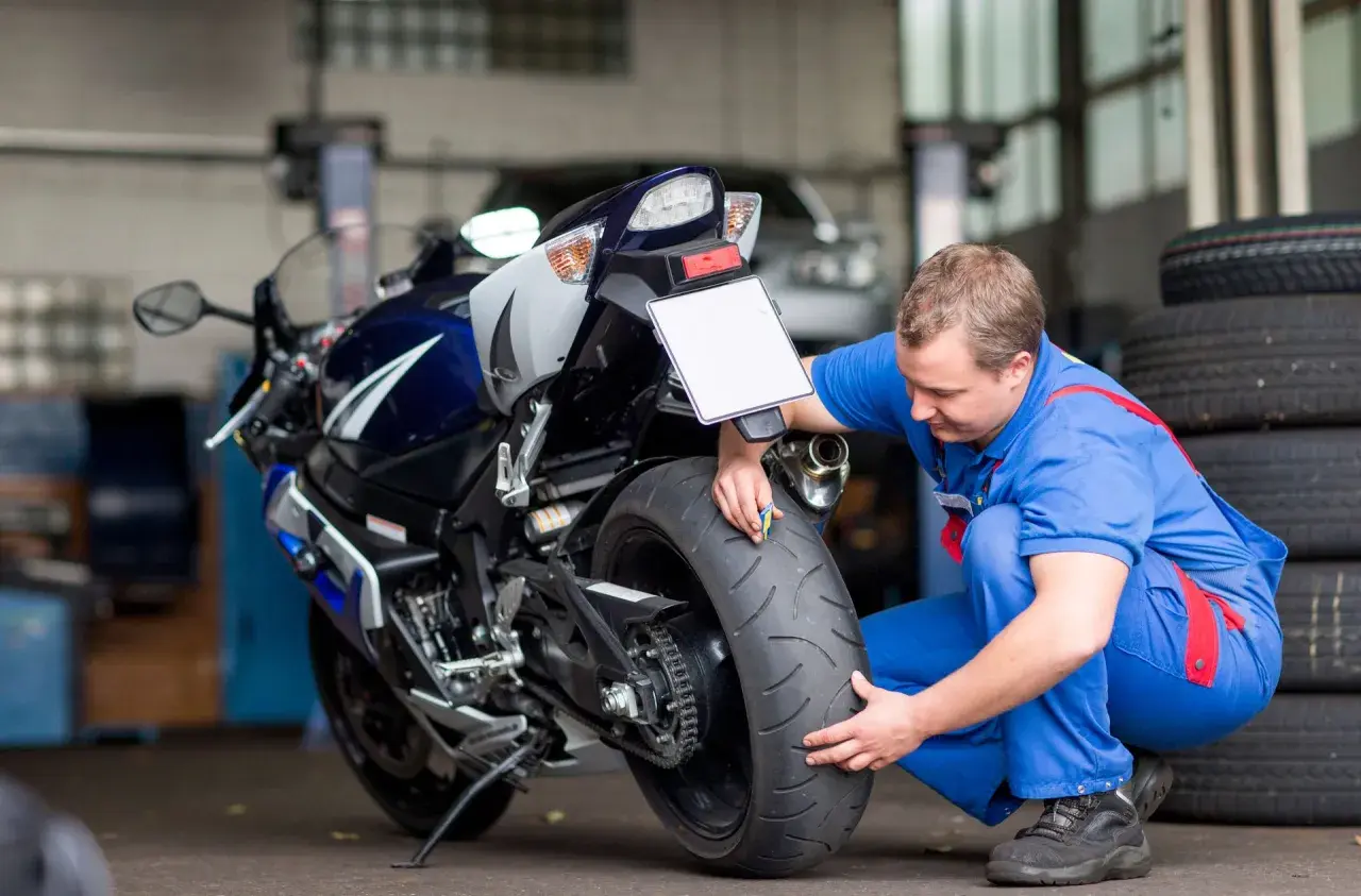 Meccanico controlla la gomma di una moto sportiva. Si chiede dopo quanti anni le gomme moto si induriscono, un problema comune per la sicurezza.