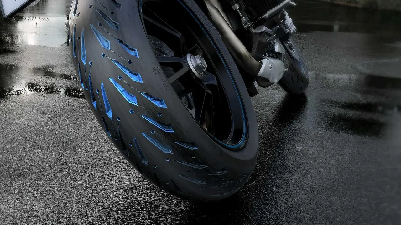 Ruota di moto con battistrada minimo e inserti blu luminosi su asfalto bagnato.