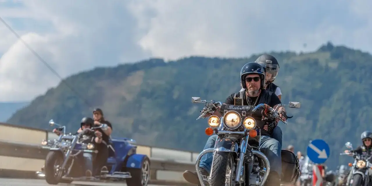 Coppie in moto e un trike sfrecciano su una strada panoramica, parte della European Bike Week.