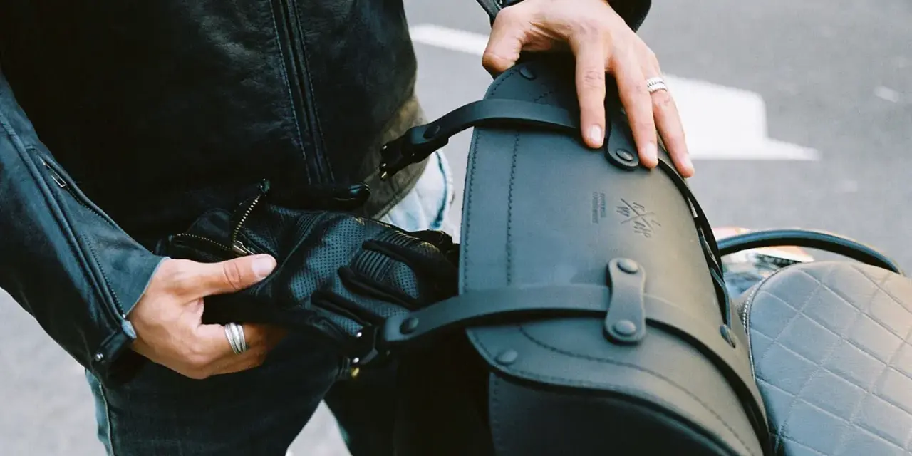 Mani che preparano il bagaglio per il portapacchi della moto. Pelle nera, guanti e cinghie per un viaggio sicuro.