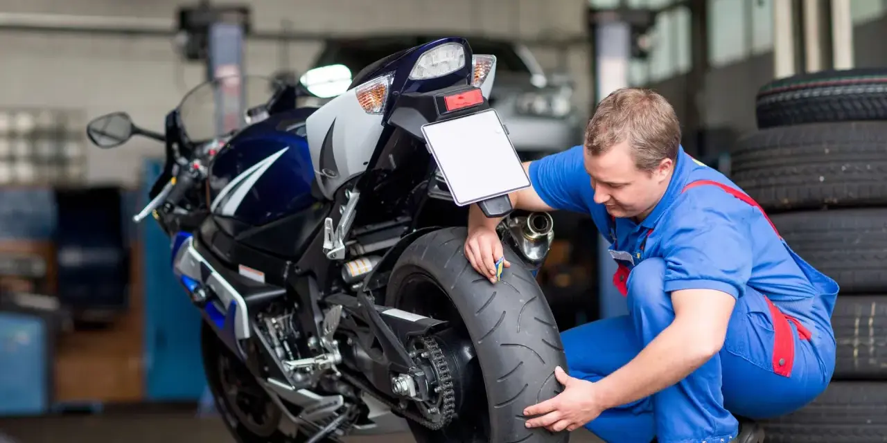 Meccanico controlla la gomma di una moto sportiva. Si chiede dopo quanti anni le gomme moto si induriscono, un problema comune per la sicurezza.