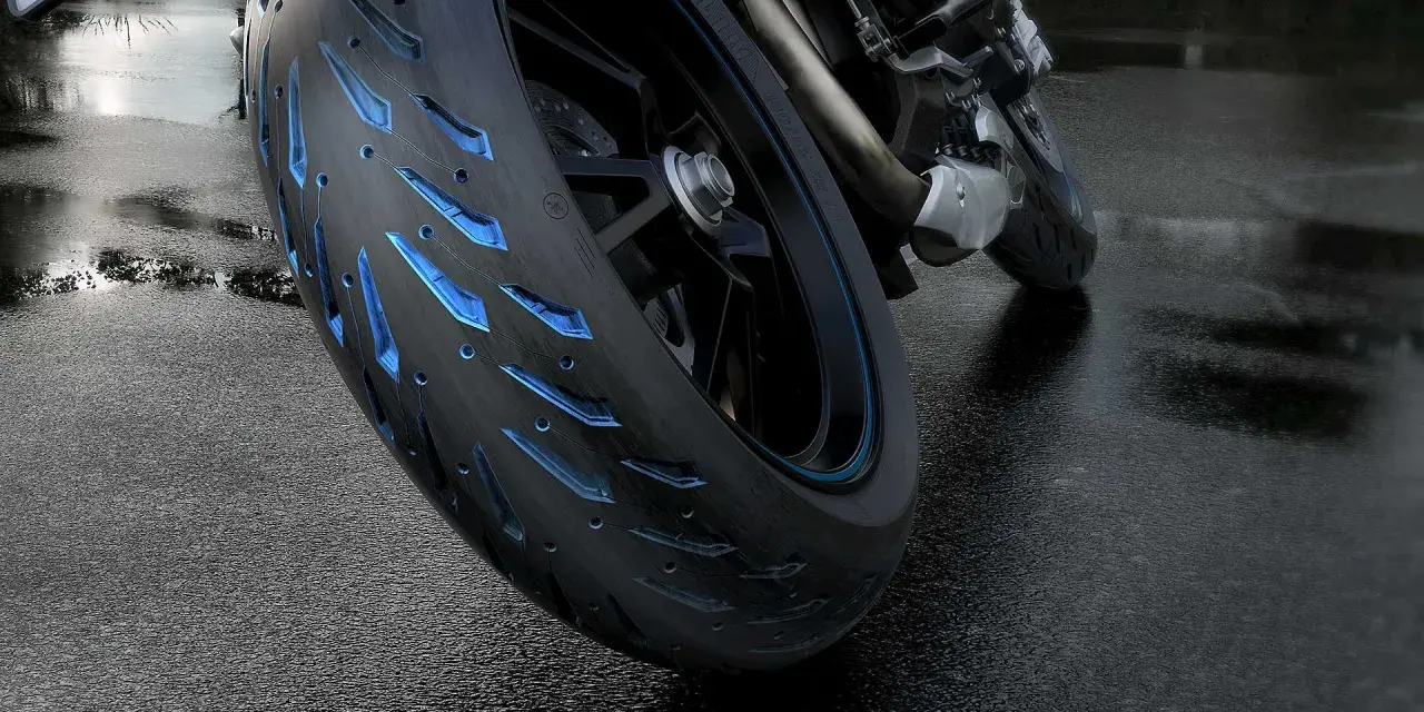 Ruota di moto con battistrada minimo e inserti blu luminosi su asfalto bagnato.