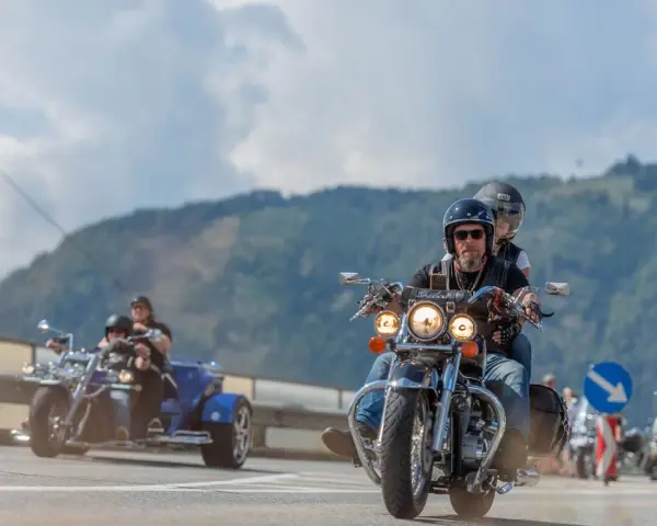 Coppie in moto e un trike sfrecciano su una strada panoramica, parte della European Bike Week.