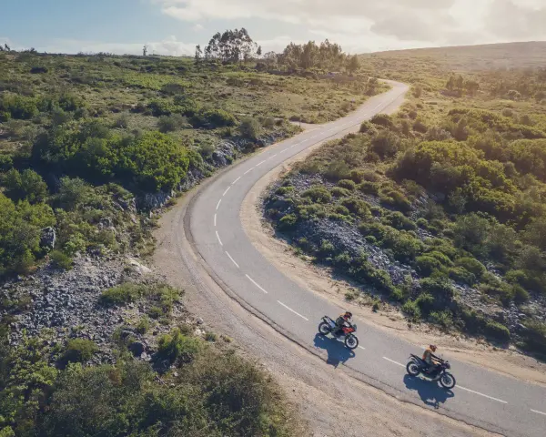 Due moto KTM sfrecciano su una strada tortuosa tra colline verdi. Un'avventura che celebra il KTM Connect.