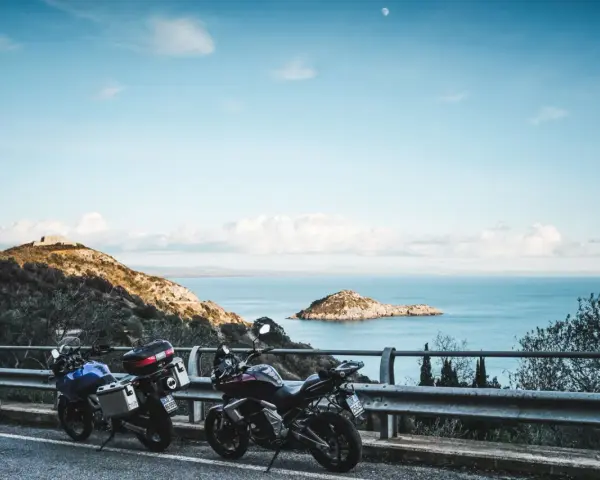 Due moto parcheggiate con vista sul mare e un'isola, con un rudere sulla collina. Un'avventura in **Argentario in moto** attende.