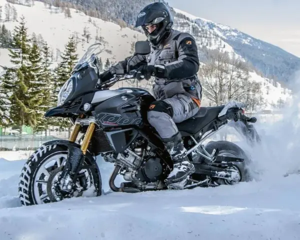 Un motociclista esperto affronta la neve fresca, dimostrando la sua abilità nell'andare in moto in inverno. La moto solleva una nuvola di neve mentre avanza.