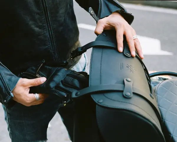 Mani che preparano il bagaglio per il portapacchi della moto. Pelle nera, guanti e cinghie per un viaggio sicuro.