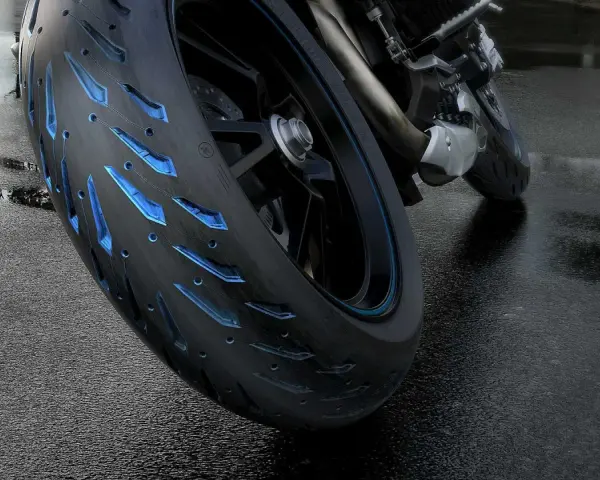Ruota di moto con battistrada minimo e inserti blu luminosi su asfalto bagnato.