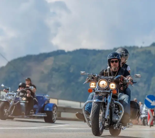 Coppie in moto e un trike sfrecciano su una strada panoramica, parte della European Bike Week.