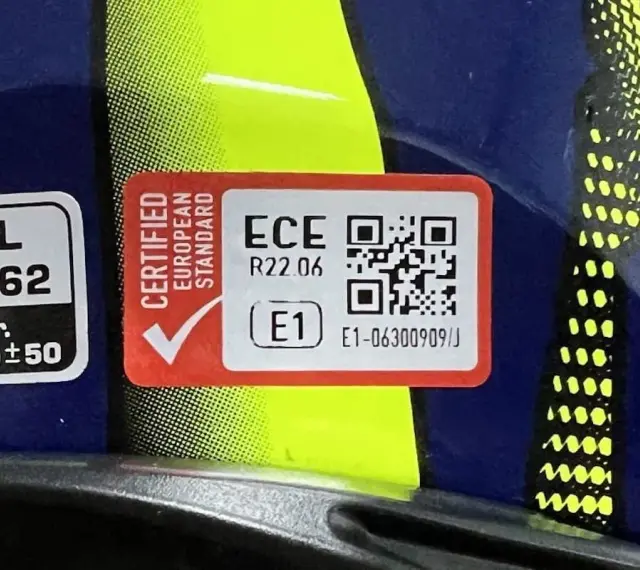 Etichetta su casco blu e giallo: "Certified European Standard", ECE R22.06, E1. Indica il **casco omologato significato** di sicurezza.