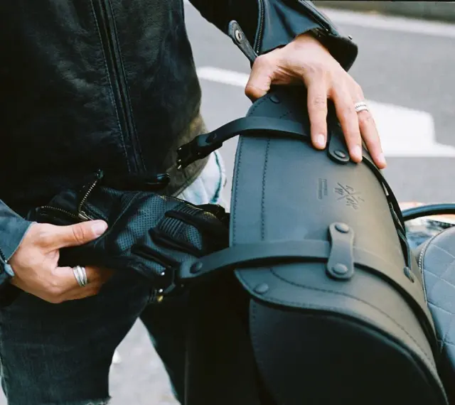 Mani che preparano il bagaglio per il portapacchi della moto. Pelle nera, guanti e cinghie per un viaggio sicuro.