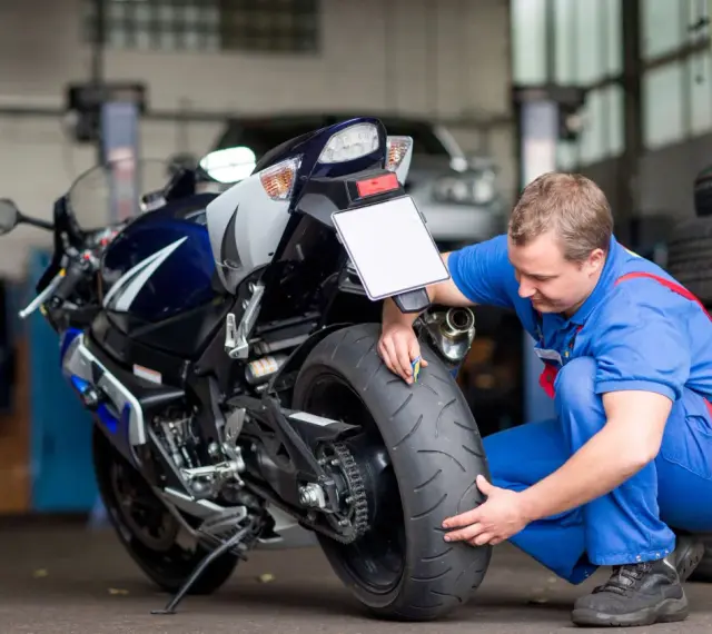 Meccanico controlla la gomma di una moto sportiva. Si chiede dopo quanti anni le gomme moto si induriscono, un problema comune per la sicurezza.