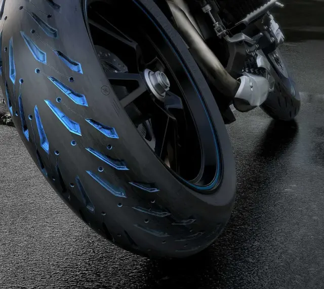 Ruota di moto con battistrada minimo e inserti blu luminosi su asfalto bagnato.