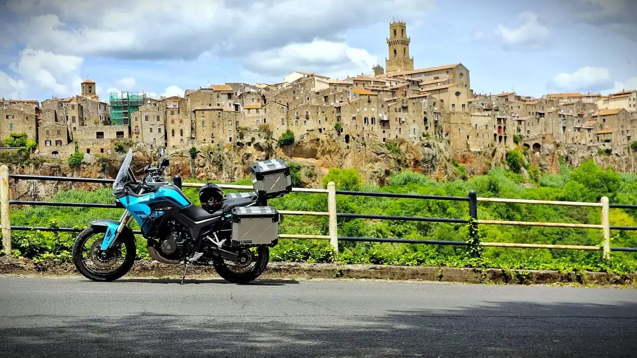 Moto blu pronta per l'avventura, con borse laterali e bauletto, sullo sfondo di un borgo arroccato. I miei compagni di viaggio in moto.