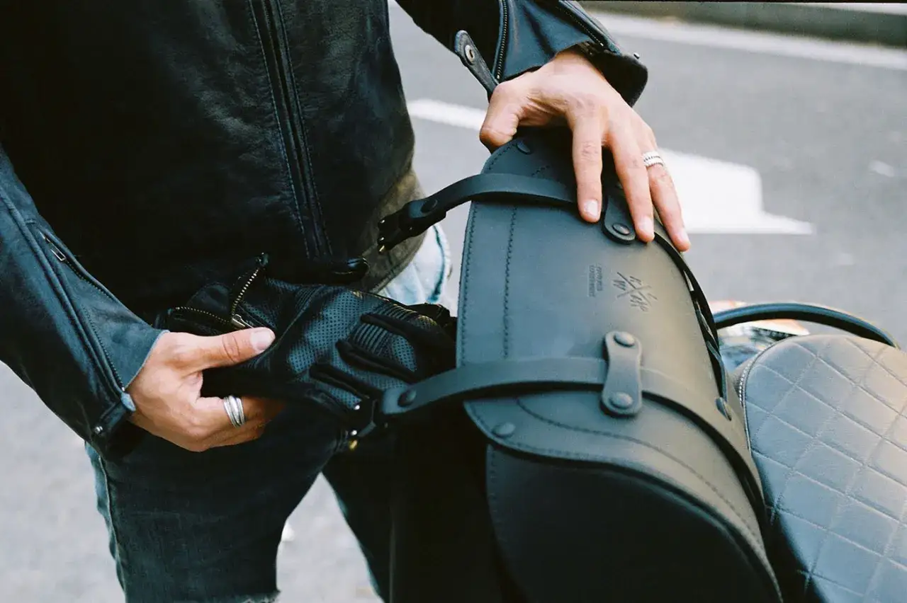 Mani che sistemano guanti in pelle e una borsa sul portapacchi di una moto, un esempio di come legare i bagagli sul portapacchi.