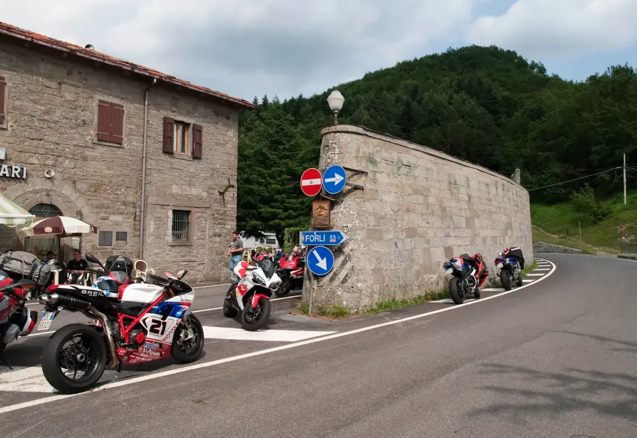 Moto sportive parcheggiate al Passo Muraglione, con un edificio in pietra e una strada tortuosa sullo sfondo.