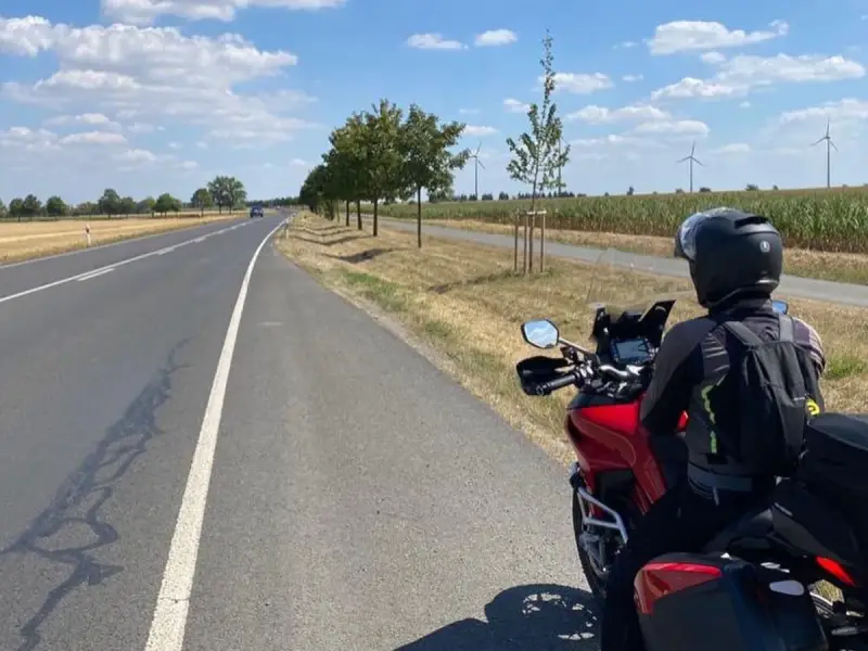 Motociclista su strada panoramica Foresta Nera, con campi di mais e pale eoliche all'orizzonte.