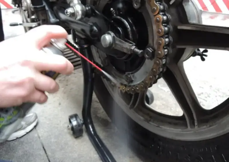Mano spruzza lubrificante sulla catena della moto. Per sapere ogni quanto ingrassare catena moto, controlla il manuale.