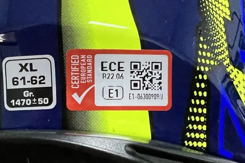Etichetta su casco blu e giallo: "Certified European Standard", ECE R22.06, E1. Indica il **casco omologato significato** di sicurezza.