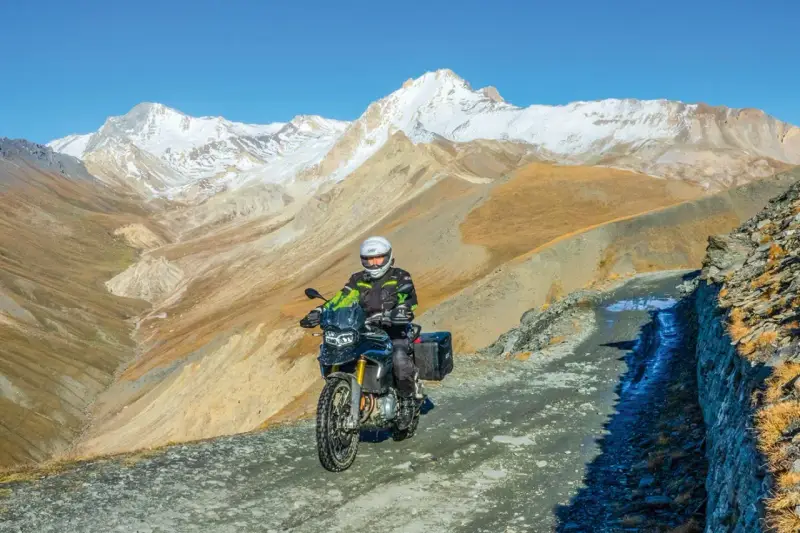 Un motociclista avventuroso affronta un sentiero impervio con la sua jafferau moto, circondato da maestose montagne innevate e paesaggi aridi.