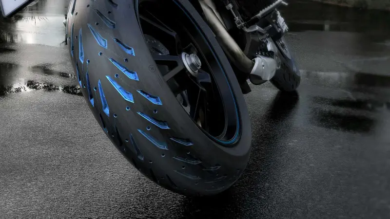 Ruota di moto con battistrada minimo e inserti blu luminosi su asfalto bagnato.